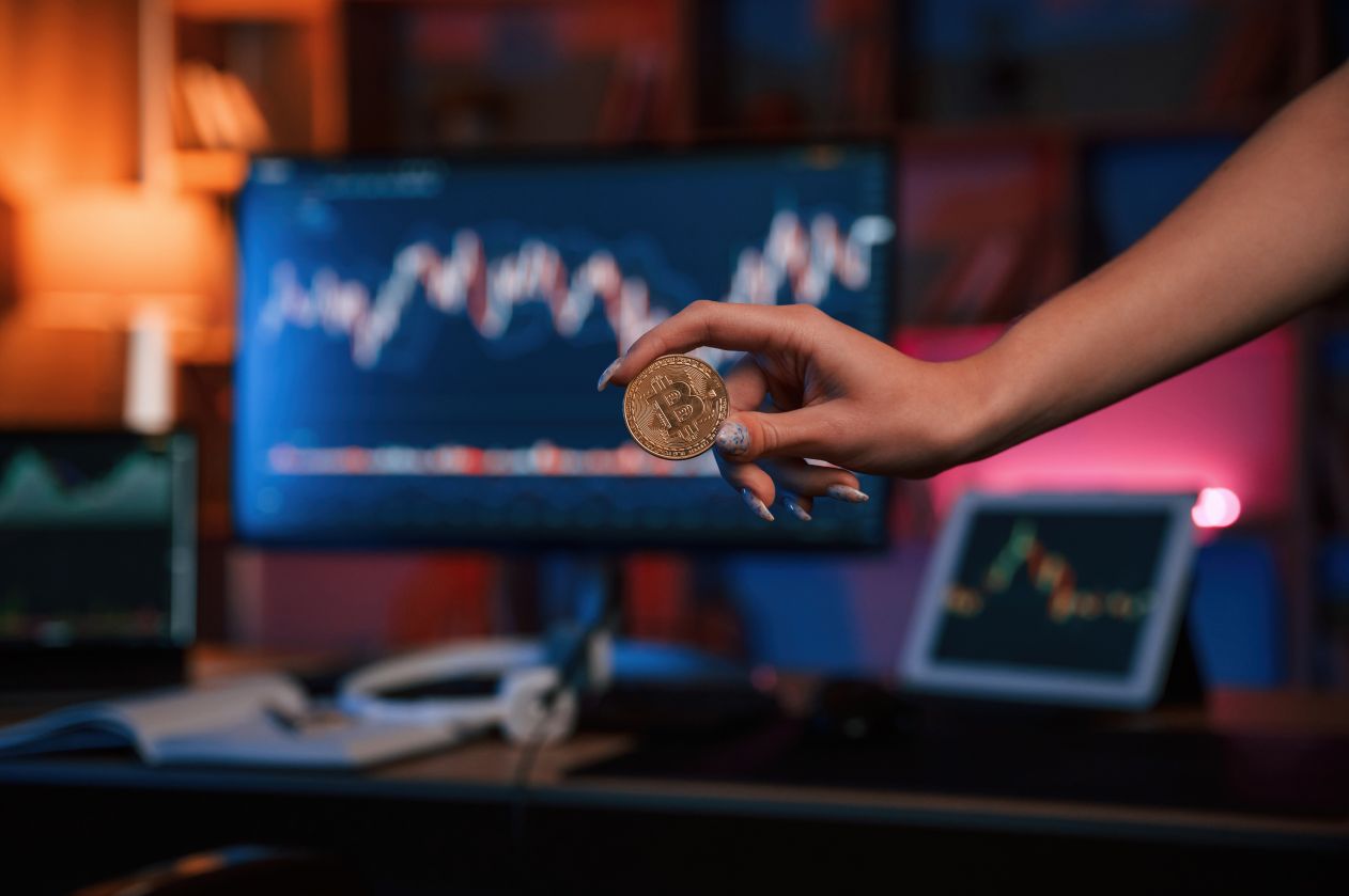 Close up view of woman's hand holding bitcoin against computer display