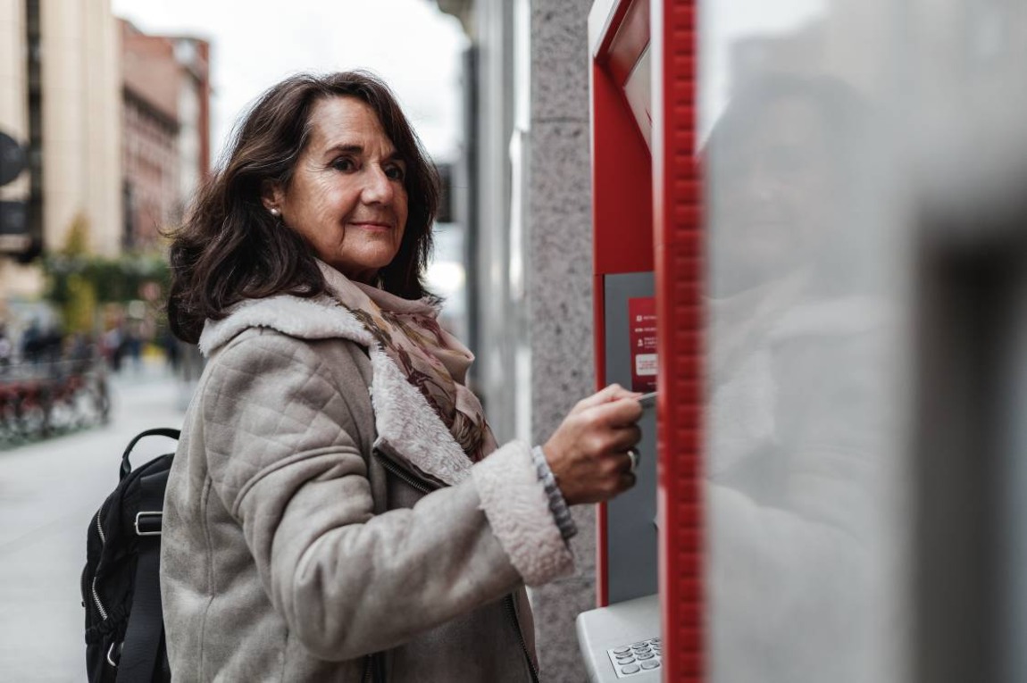 Closeup view of smiling woman introducing credit card in traditional ATM banking