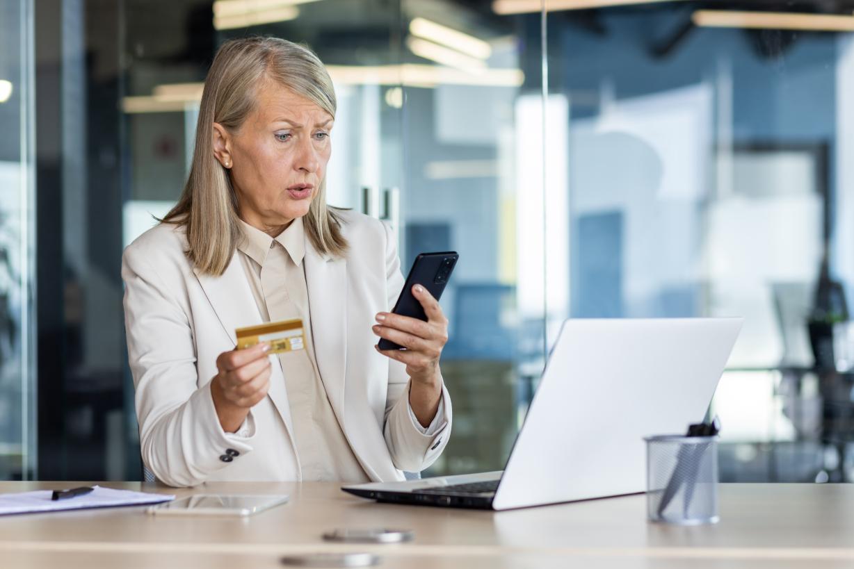 Confused senior businesswoman sitting at the desk in the office in a business suit