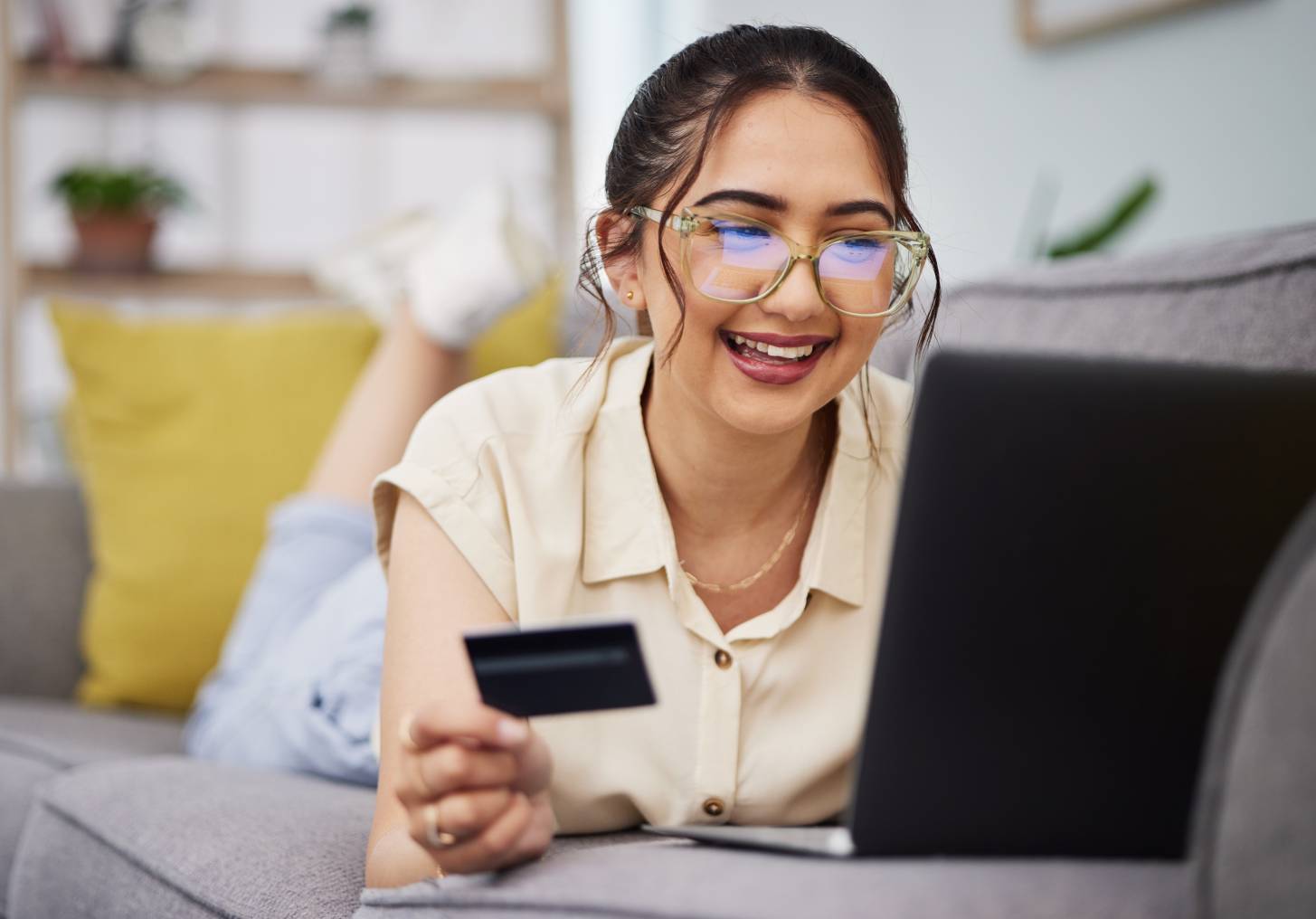 Happy woman, credit card and money with laptop on sofa