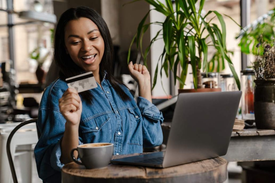 Happy young woman holding credit card and doing digital banking