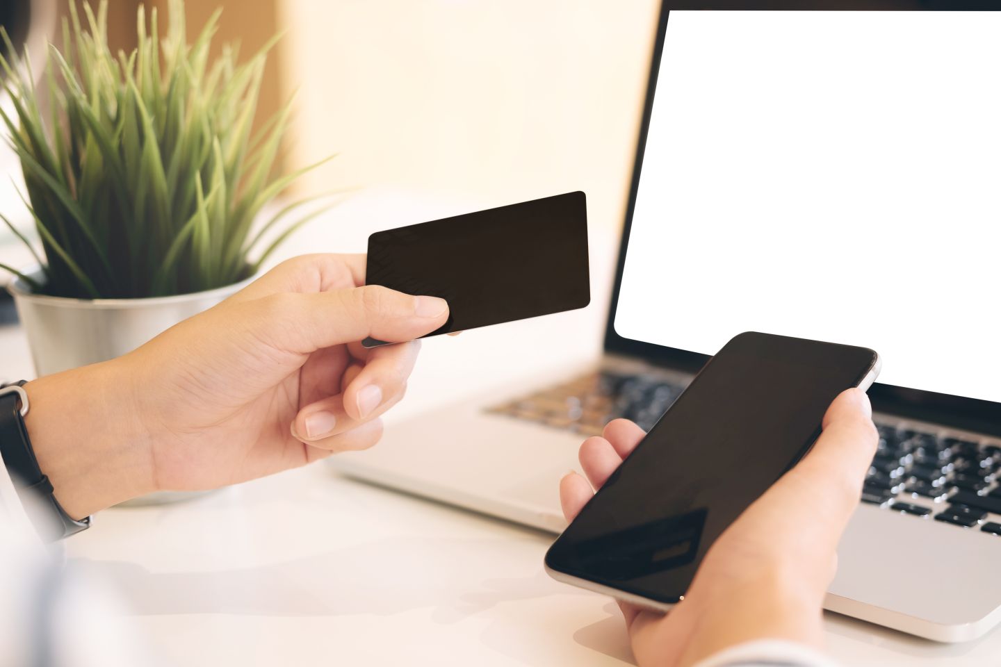 Online payment - woman's hands holding smartphone and using credit card for payment in front of a laptop