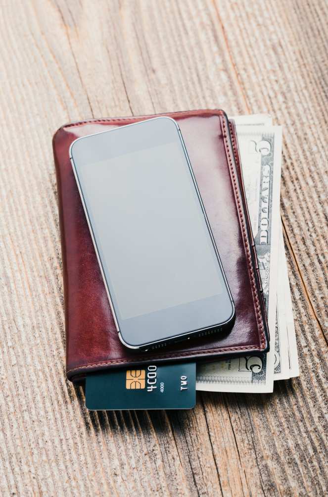 Smartphone with blank screen, wallet, dollar banknotes, debit credit cards and notebook on table