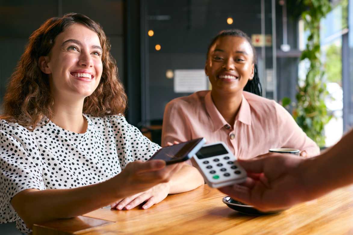 Woman In Coffee Shop Paying Bill With Contactless Mobile Phone Payment