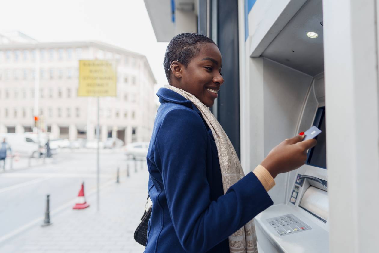 Young african woman withdrawing cash at the ATM using her offshore bank account