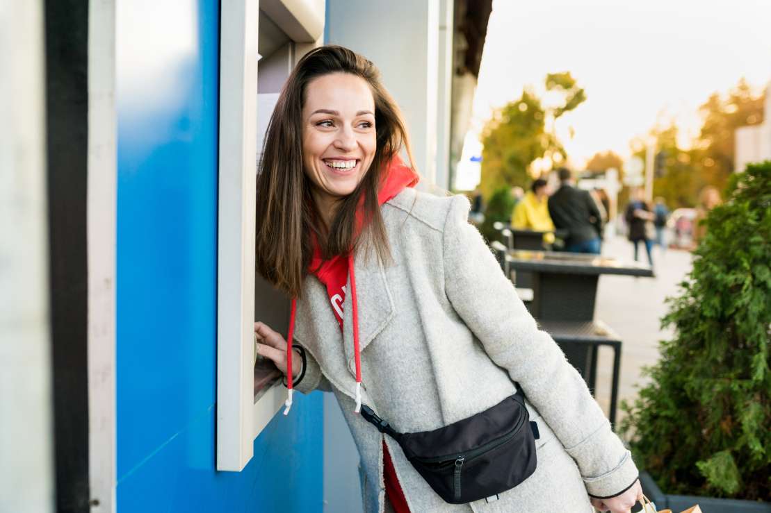 Junge Br&uuml;nette Frau steckt Kreditkarte ein und hebt Geld an Geldautomaten im Freien ab.
